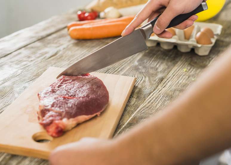 Homem usando tábua de corte para preparar carne vermelha.