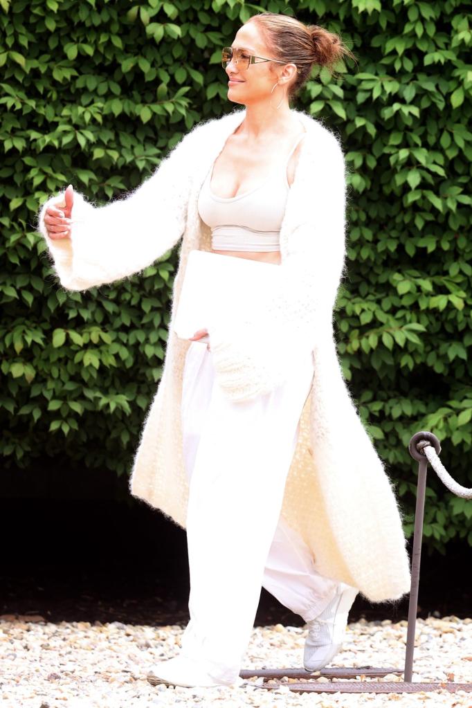 Jennifer Lopez in a soft, long sweater, over a sports bra and white trousers in the Hamptons.