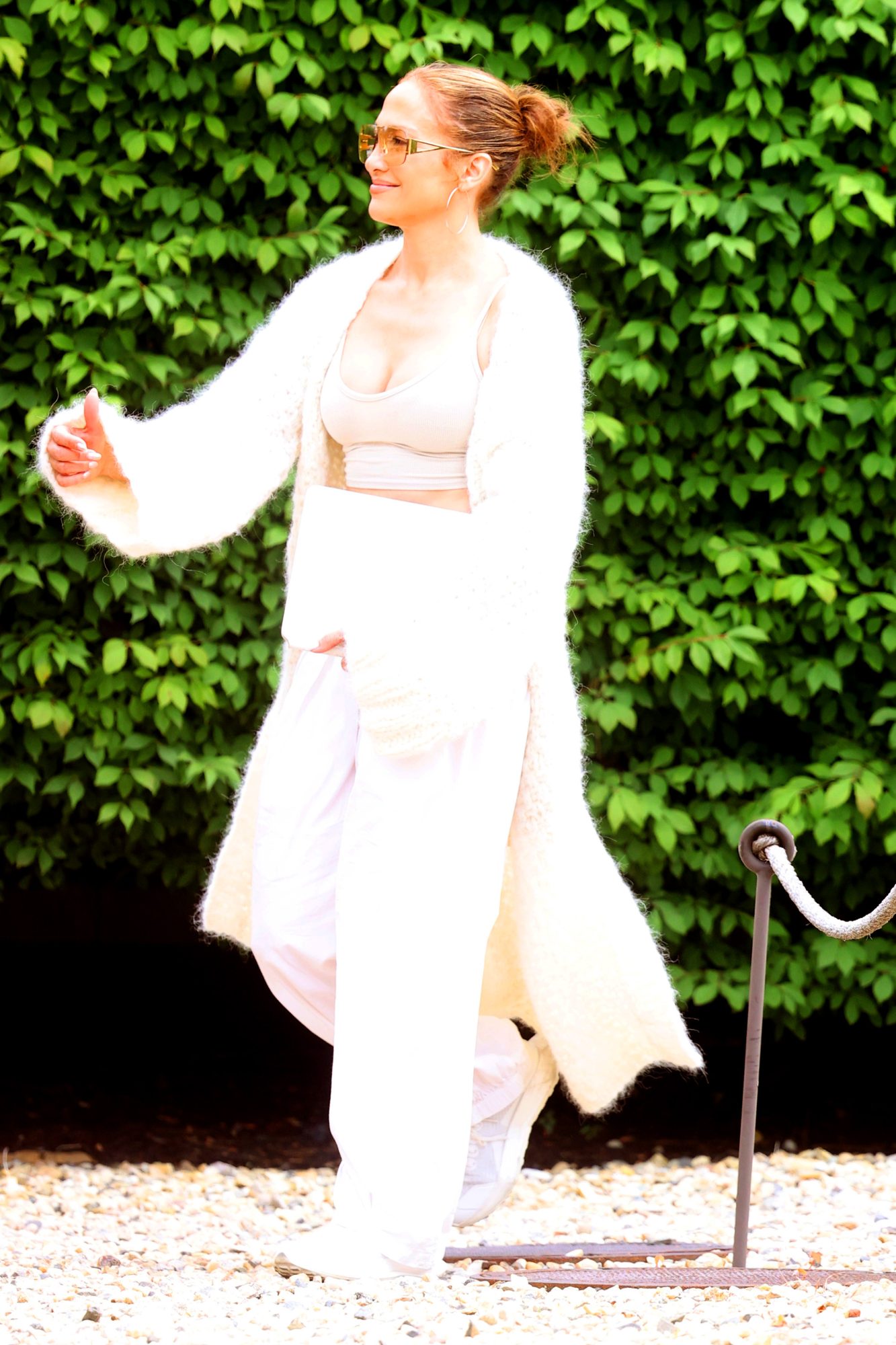 Jennifer Lopez in a soft, long sweater, over a sports bra and white trousers in the Hamptons.