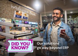 Smiling man holding a phone and a coffee cup inside a convenience store with a display of sandwiches in the background. Text overlay reads 'Did You Know? Our solutions go way beyond ERP.'