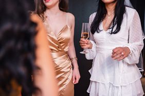 Close-up of an unrecognizable female holding a glass of champagne during her bachelorette party. She is dressed in a white dress and wearing a veil since she is about to get married soon