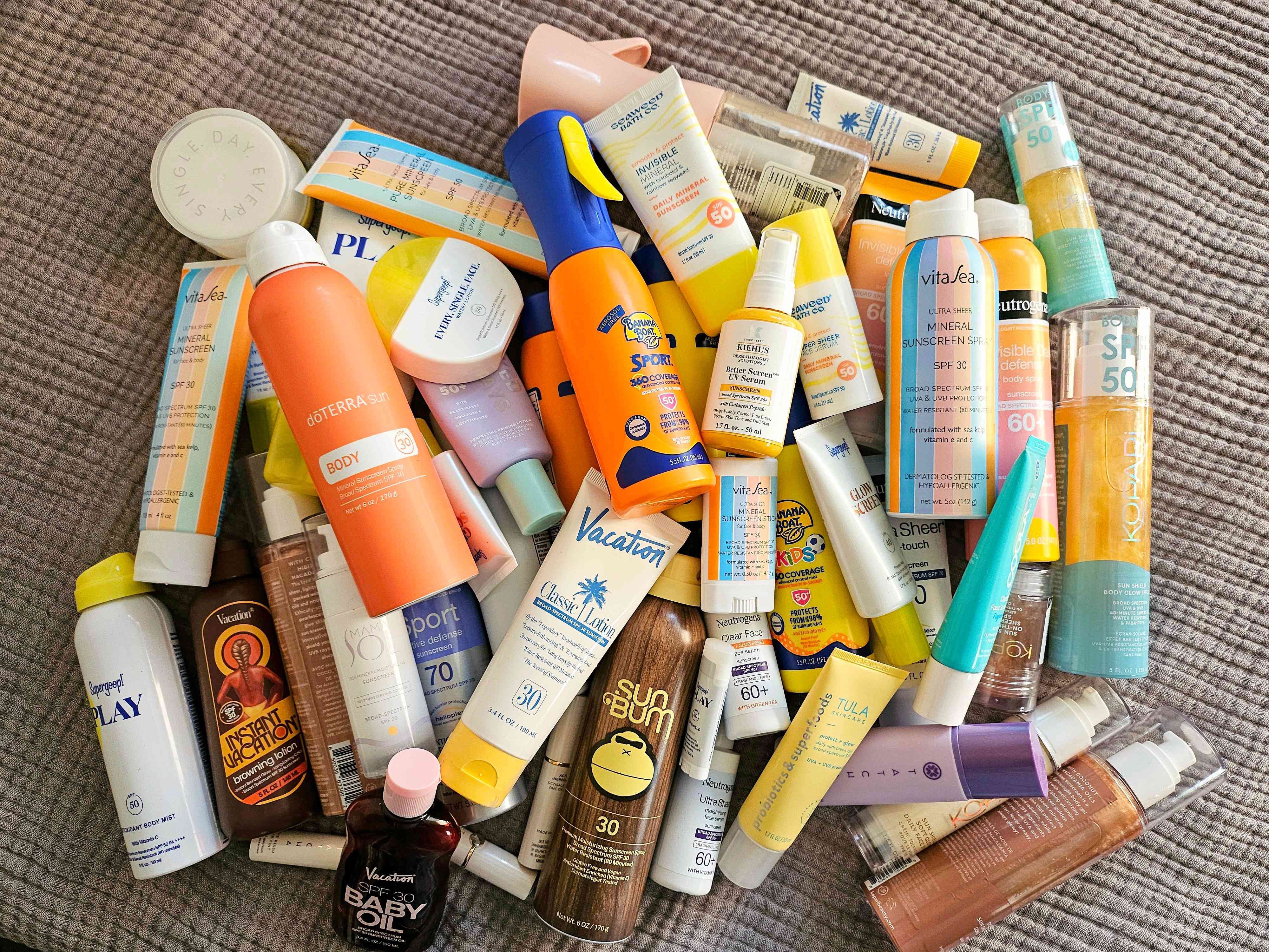 A pile of a variety of sunscreen placed on a blanket 