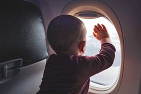 A baby looking out an aeroplane window with their hands against the glass.