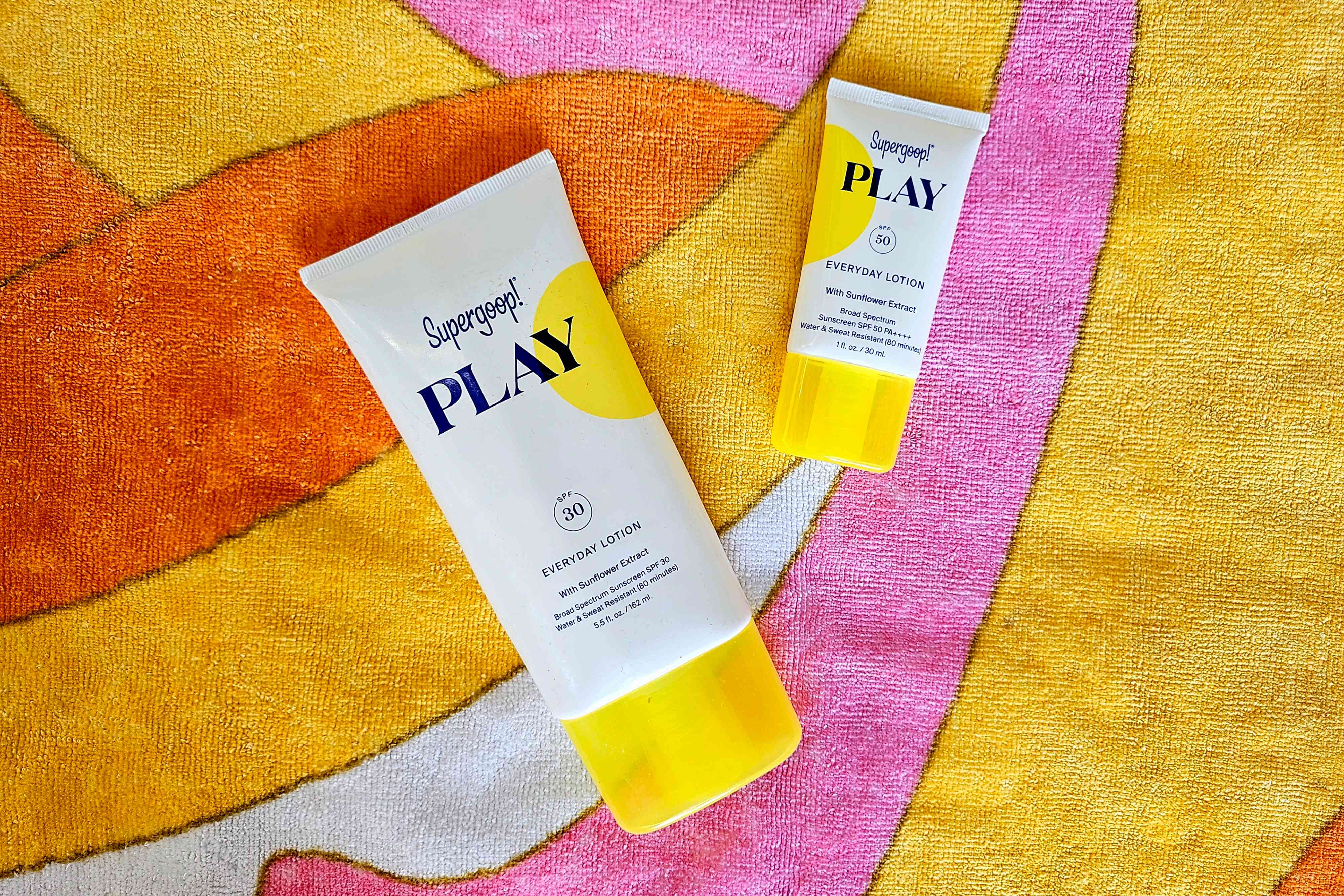 Supergoop Play lotion in 5.5 ounces and 2.4 ounces on a colorful beach towel