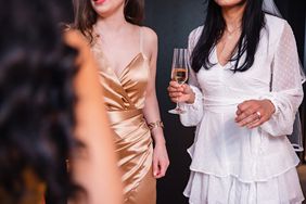 STOCK Close-up of an unrecognizable female holding a glass of champagne during her bachelorette party. She is dressed in a white dress and wearing a veil since she is about to get married soon.