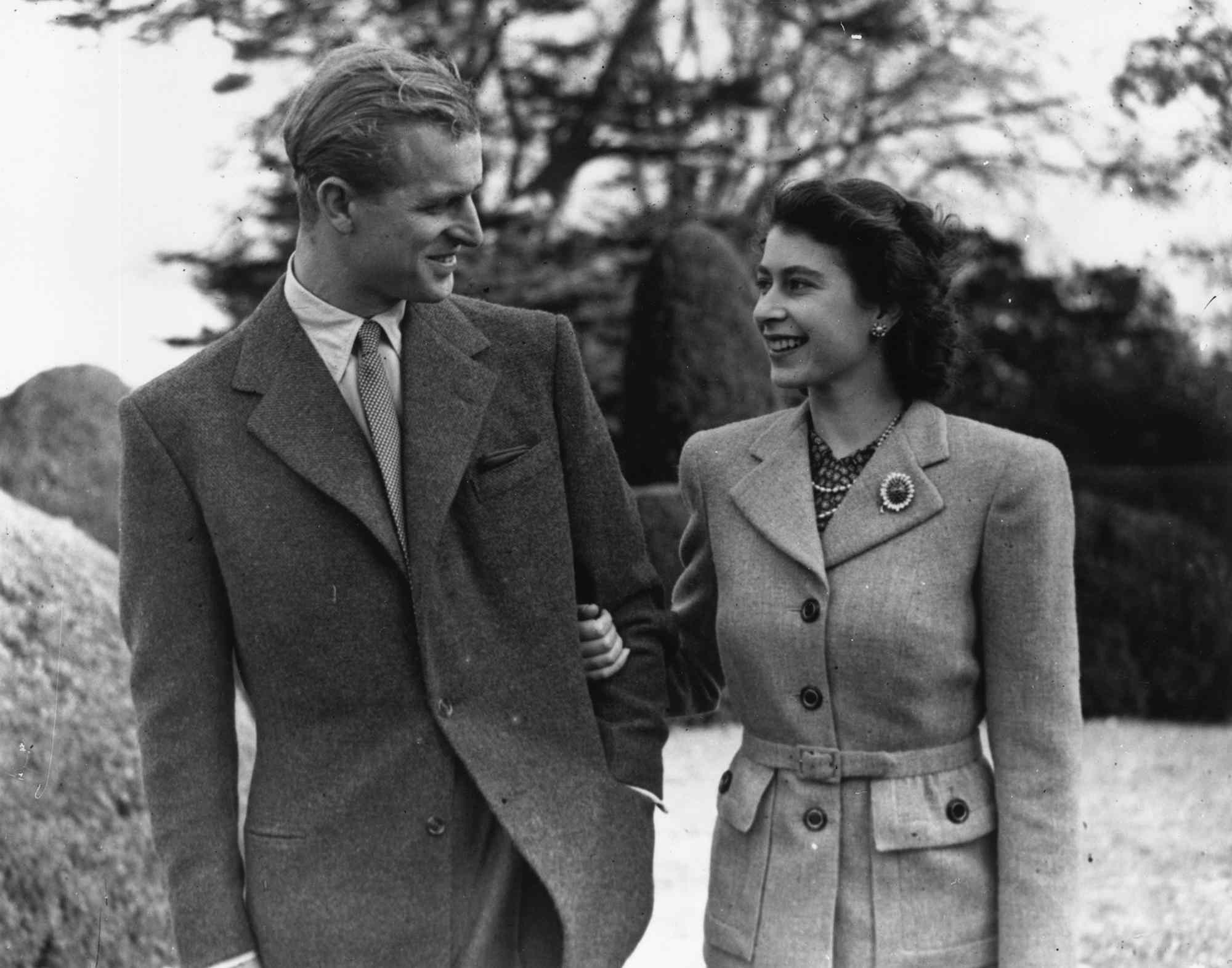 Prince Philip and Queen Elizabeth smile at one another while walking arm-in-arm outside.