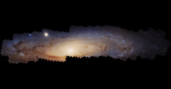 A composite image of the Andromeda Galaxy showing a bright, glowing core surrounded by spiral arms with stars and cosmic dust against a dark background. The galaxy stretches horizontally across the image.