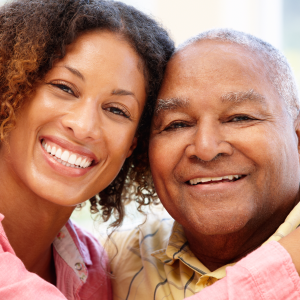 A Black father and his adult daughter, hugging and smiling at the camera.