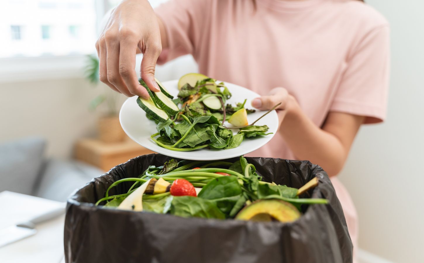 A woman throwing salad items and vegetables into a bin, contributing to food waste