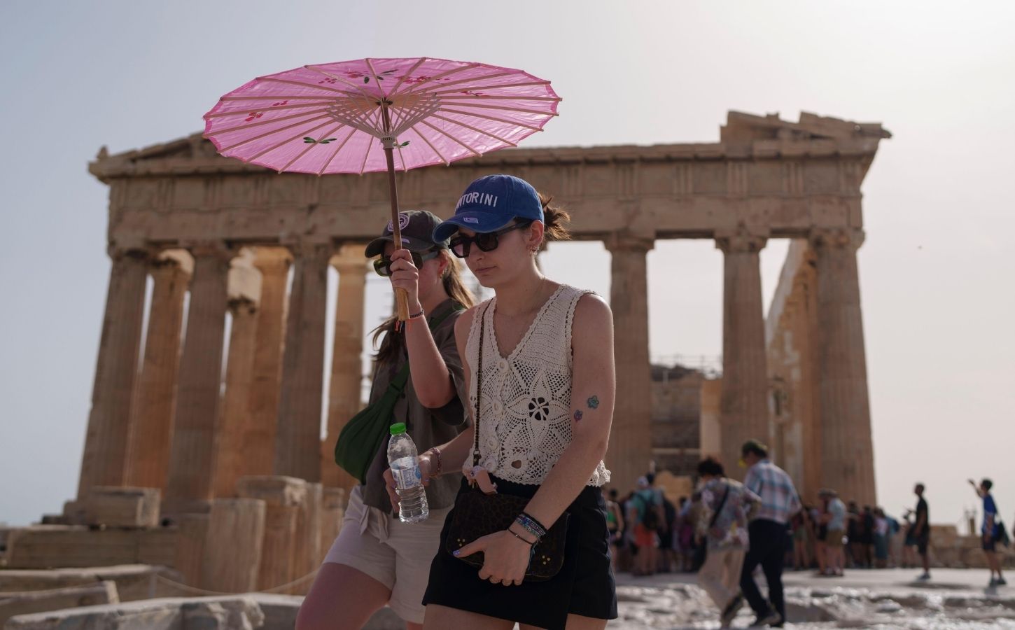 Two people walking by the Acropolis in Athens during a heatwave carrying a pink umbrella