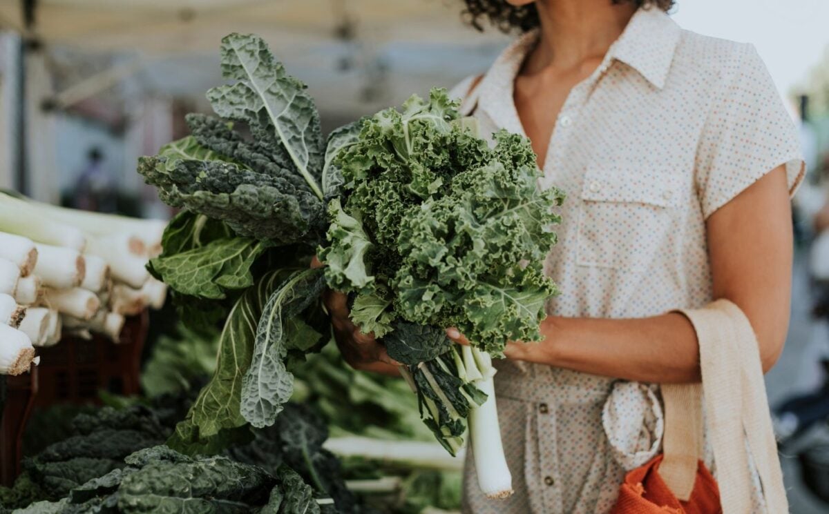 Photo shows a woman shopping and holding a large bunch of fresh kale, which is one of the top sources of plant-based calcium