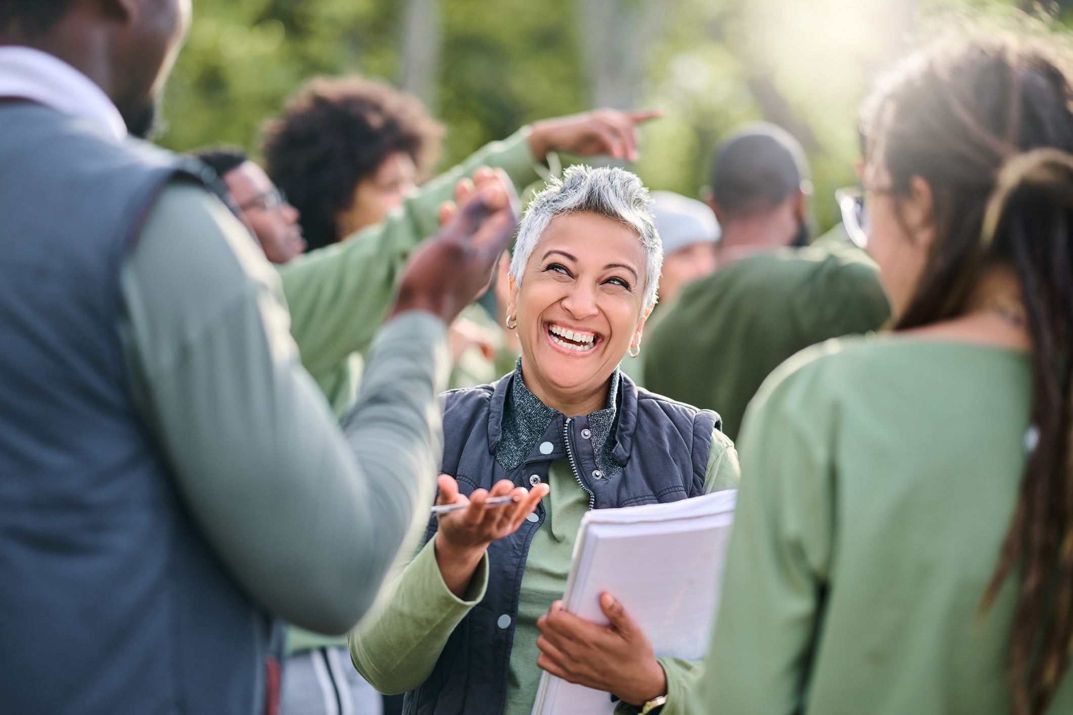 Photo of a female community volunteer carrying a sign up sheet, interacting with other volunteers.