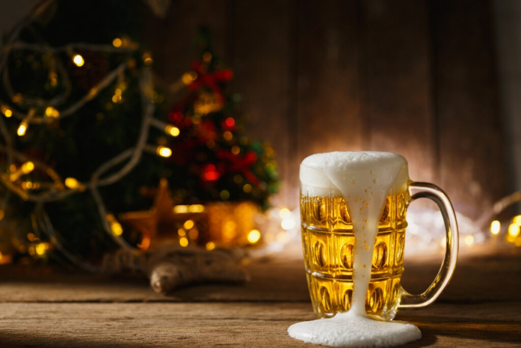 Caneca de vidro com cerveja saindo do copo em cima de mesa de madeira e atrás arvore de natal