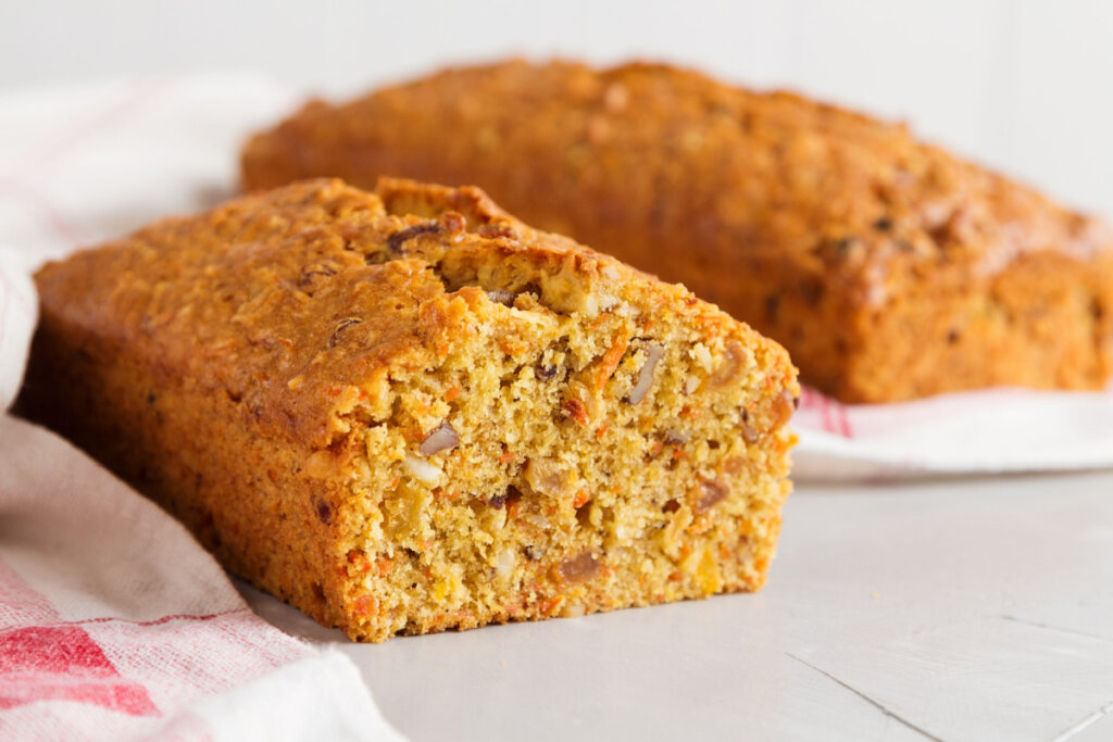 Bolo de cenoura e nozes cortada ao meio com bolo inteiro ao fundo