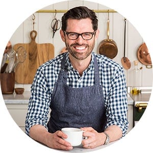 Photo of John Kanell holding a coffee cup in the kitchen.	