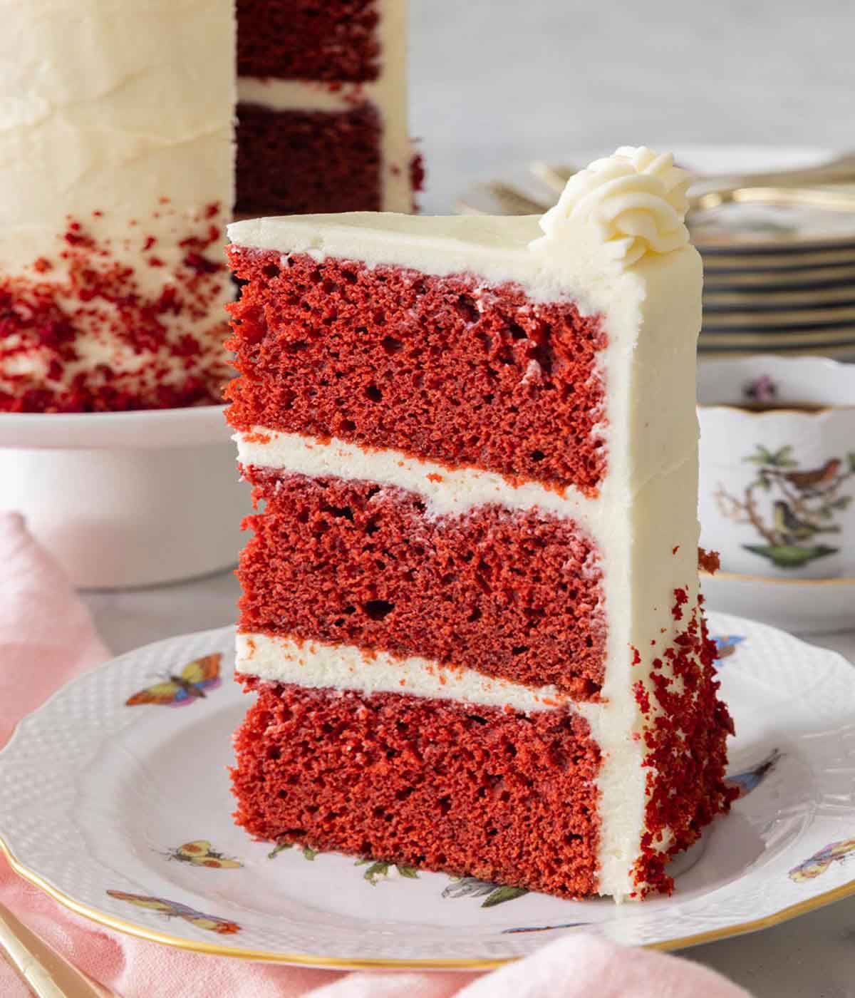 A slice of red velvet cake showing the three layers with frosting in-between.