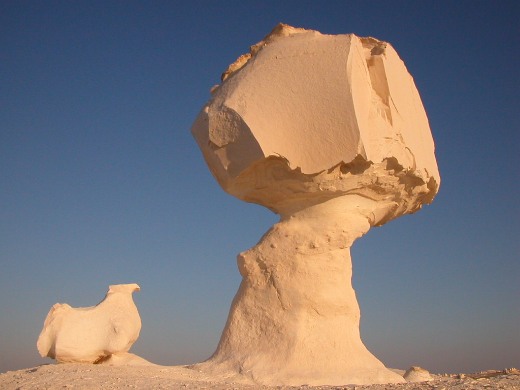 Column of sand with larger sand boulder capping the column; the boulder has multiple flattened and faceted surfaces.