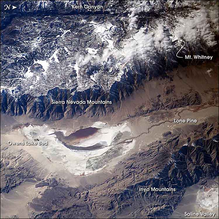 Photo taken from the ISS showing the Sierra Nevada Mountains running from left to right; the mountain range on the upward side of the image are snow capped while the mountain slopes and basin at the base of the range on the downward side of the image are tan and lack vegetation, indicating a rain shadow. The Inyo Mountains are near the bottom of the photo which lack snow due to the rain shadow.