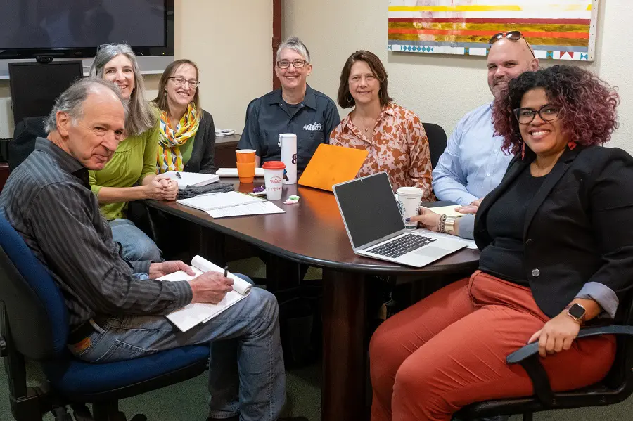 A diverse group of current and former small business owners in a conference room discussing the benefits of employee ownership