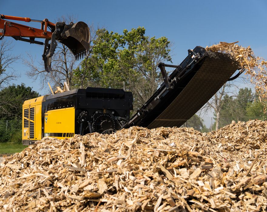 An image of a shredder with a pile of mulch in front of it