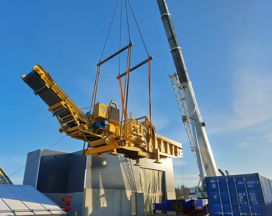 A yellow Vermeer wood grinder is lifted into the air by a crane.