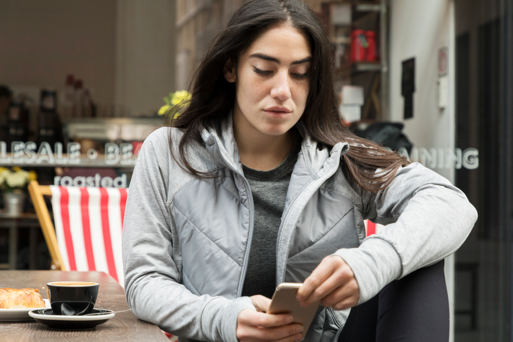 A woman sits and looks at her phone