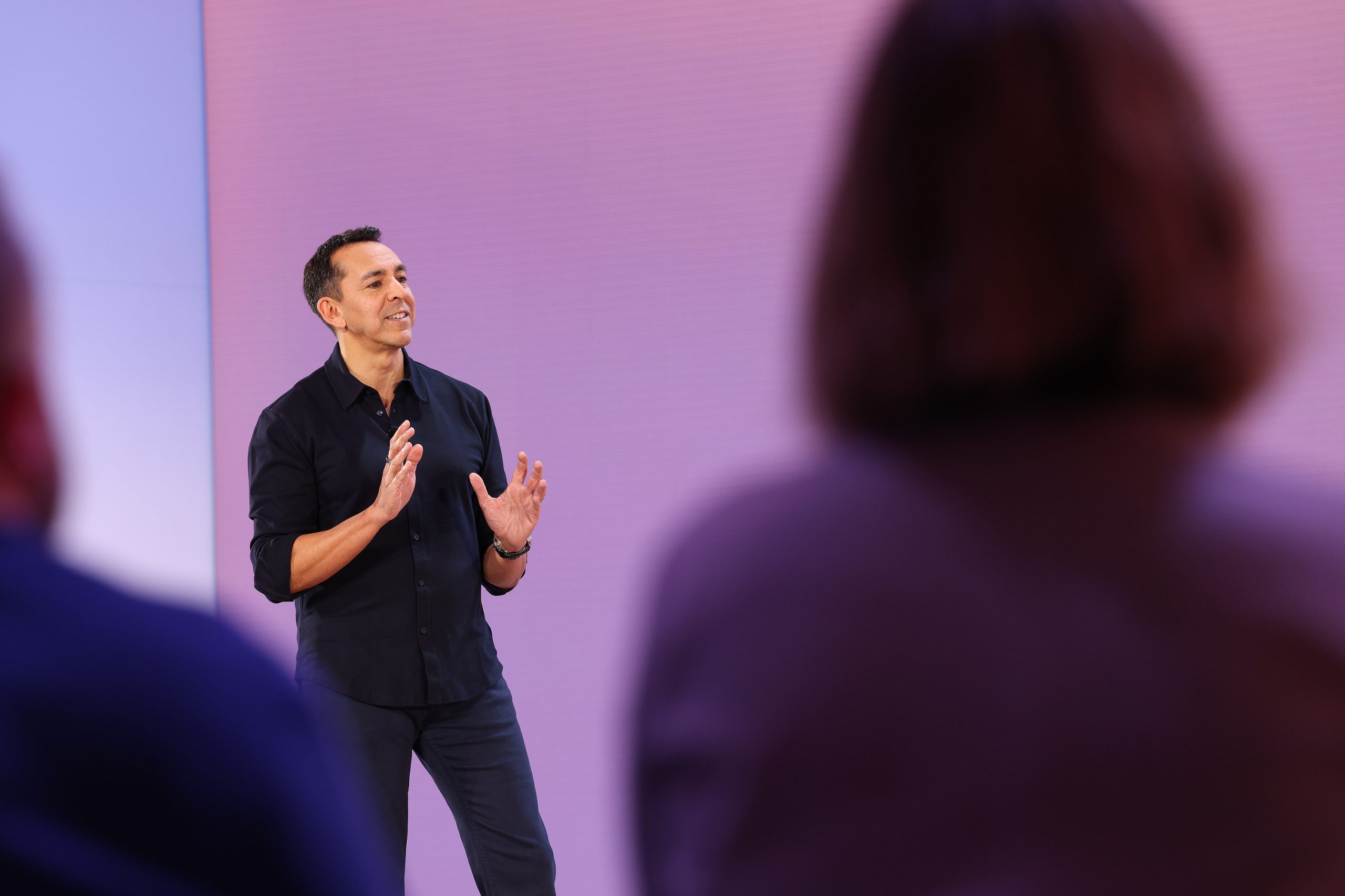 A man standing on stage in front of an audience with a purple screen behind him