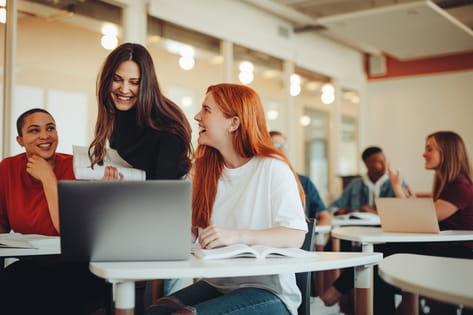 A group of three female students smile at a laptop in a university seminar group project