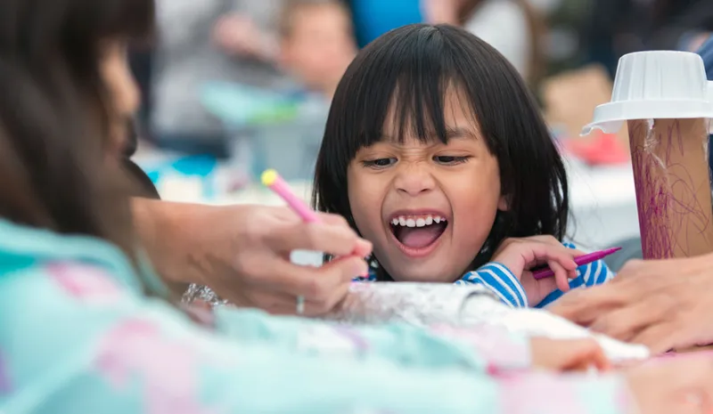 A smiling child at a table with colouring pencils