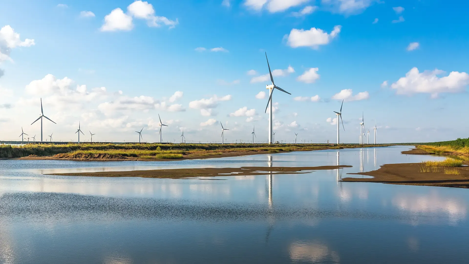 Wind turbines against a blue sky reflected in ground water