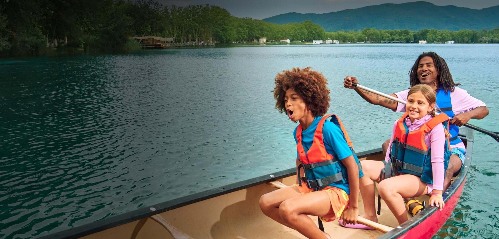 Two children and one adult laugh while canoeing across a lake. 