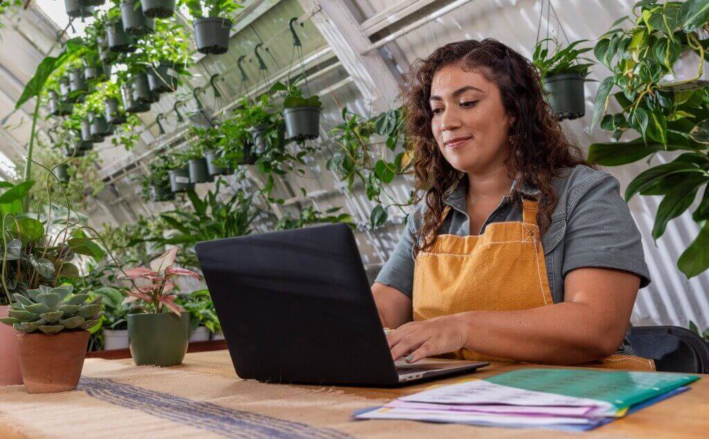 Owner of a plant store sitting at table working on her laptop.