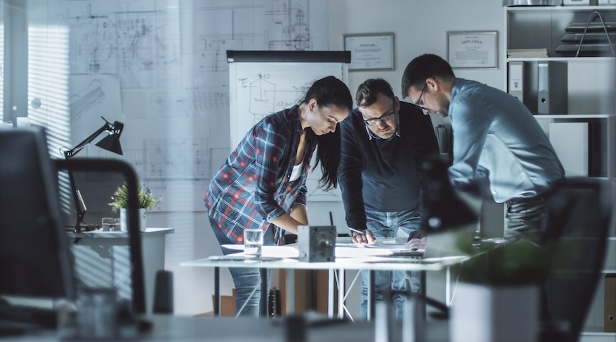 Three people are working on a laptop in a conference room.