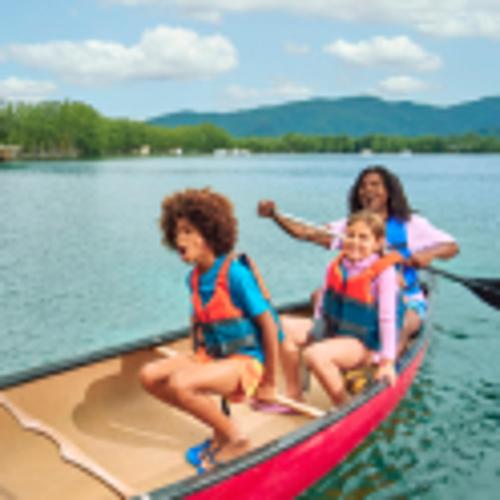 Two children and one adult laugh while canoeing across a lake. 