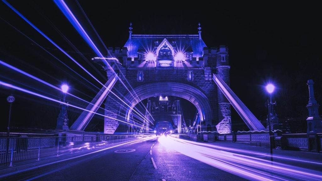 Illuminated bridge at night with light trails from passing vehicles.