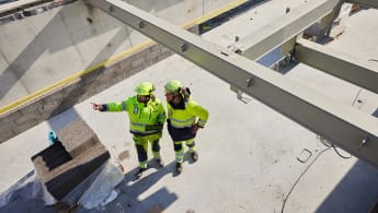 Två medarbetare som står i en byggarbetsplats. Den ena pekar mot en riktning.