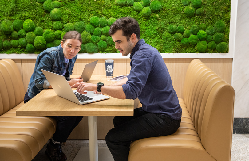 Two Orchard employees working in a booth near the moss wall in the NYC office