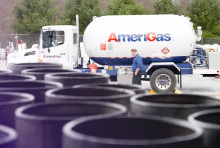 A man stands next to an AmeriGas propane truck in an outdoor setting, with large industrial pipes in the foreground.