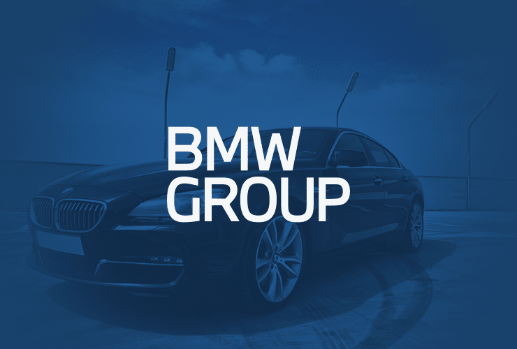 A dark colored BMW car is shown with "BMW Group" text overlaying the image. The background features a clear blue sky and streetlights.