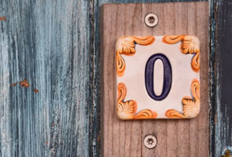 A ceramic tile with the number "0" is mounted on a wooden wall. The tile has a decorative border with orange and yellow patterns.