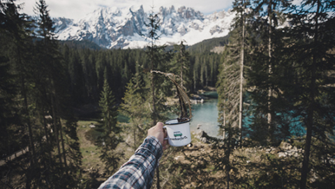 coffee spilling from a roadsurfer cup with lake and forest in the background