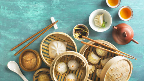 Assorted Chinese food dim sum, steamed bun, dumpling and traditional tea set on green textured table top. Flat lay overhead view text space image.