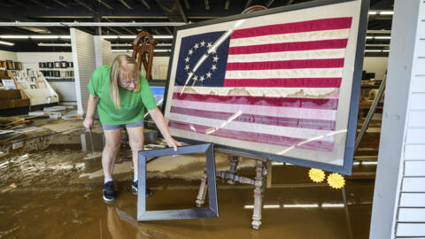 Une femme se tient à côté d'un drapeau américain alors qu'elle nettoie un atelier endommagé par les eaux des crue de l'ouragan Hélène sur North Green Street, le lundi 30 septembre 2024, à Morganton, en Caroline du Nord.