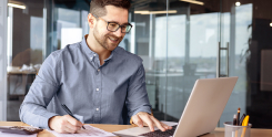 homem branco usando óculos e camisa azul mexendo no notebook