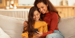 mãe e filha sentadas no sófa mexendo no celular