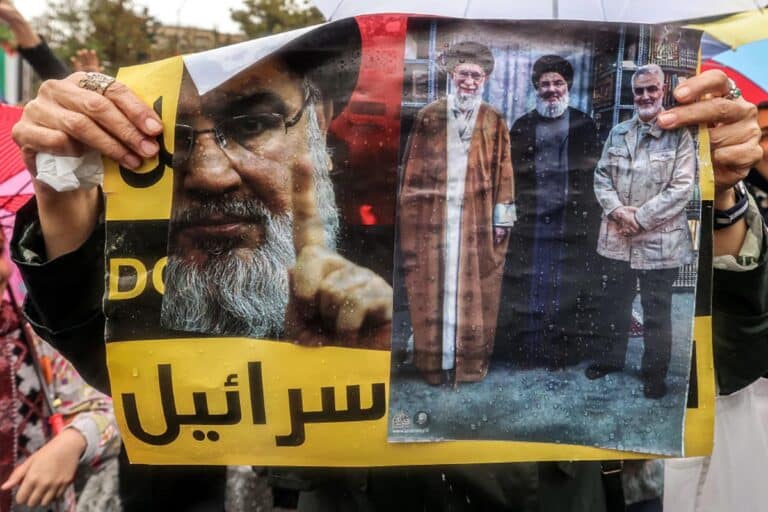 A demonstrator stands in the rain holding a picture depicting (L to R) Iran's Supreme Leader Ali Khamenei; late Lebanese Hezbollah leader Hassan Nasrallah who was killed by an Israeli air strike on September 27, 2024; and Iran's Islamic Revolutionary Guard Corps' (IRGC) Quds Force commander Qasem Soleimani who was killed by a US drone strike in January 2020; during an anti-Israel protest in Tehran's Palestine Square on September 28, 2024.