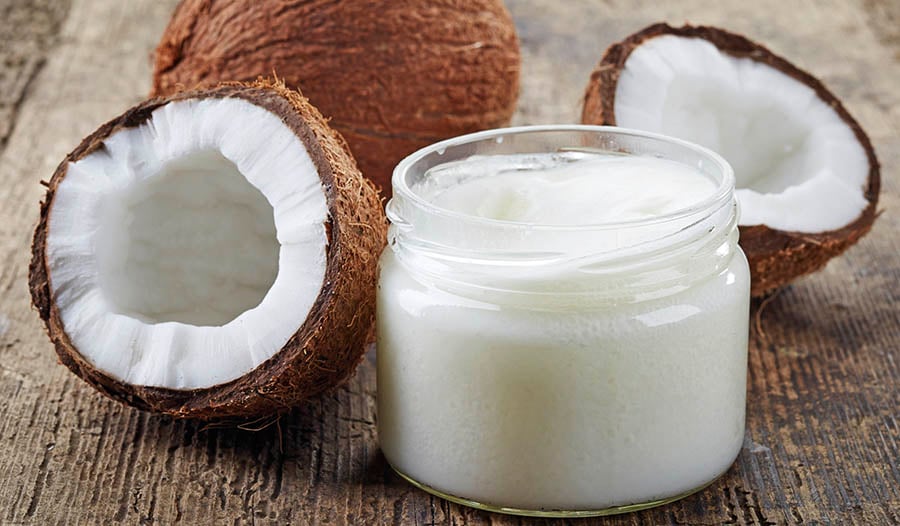 Coconut oil in jar with coconuts on wooden table