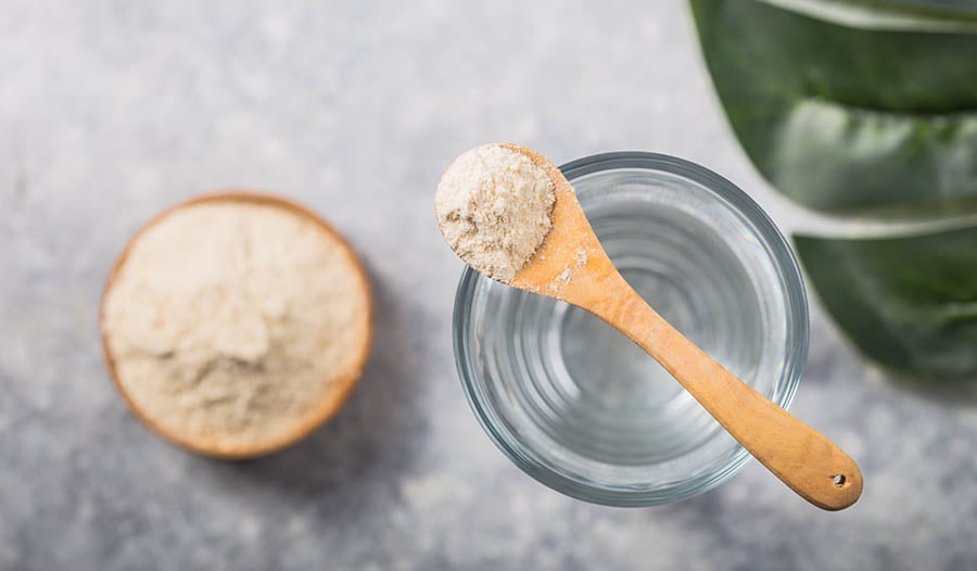 Collagen powder in wooden spoon with bowl and glass of water