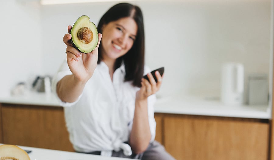 Healthy woman holding an avocado in kitchen