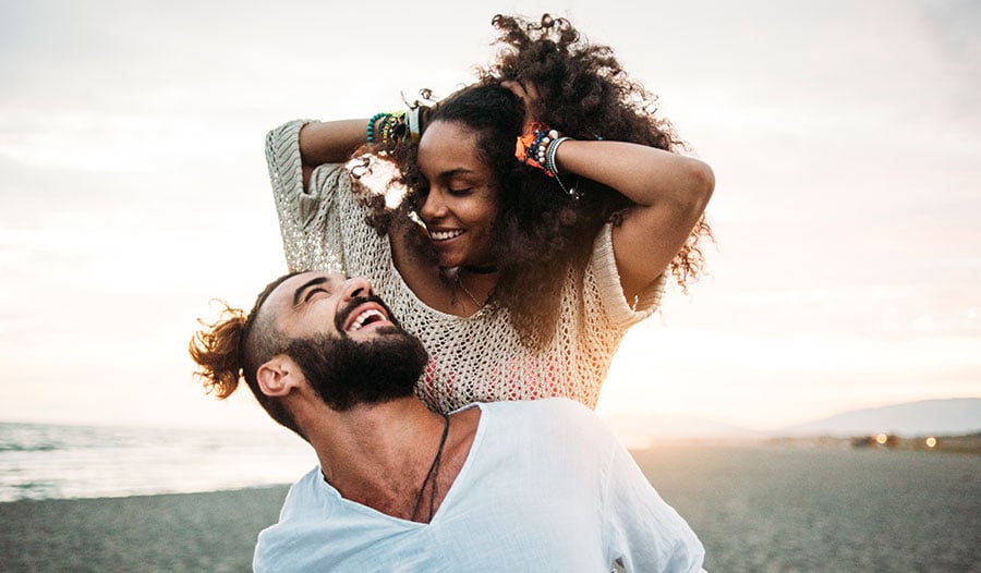 man and woman holding her hair back on the beach smiling at each other